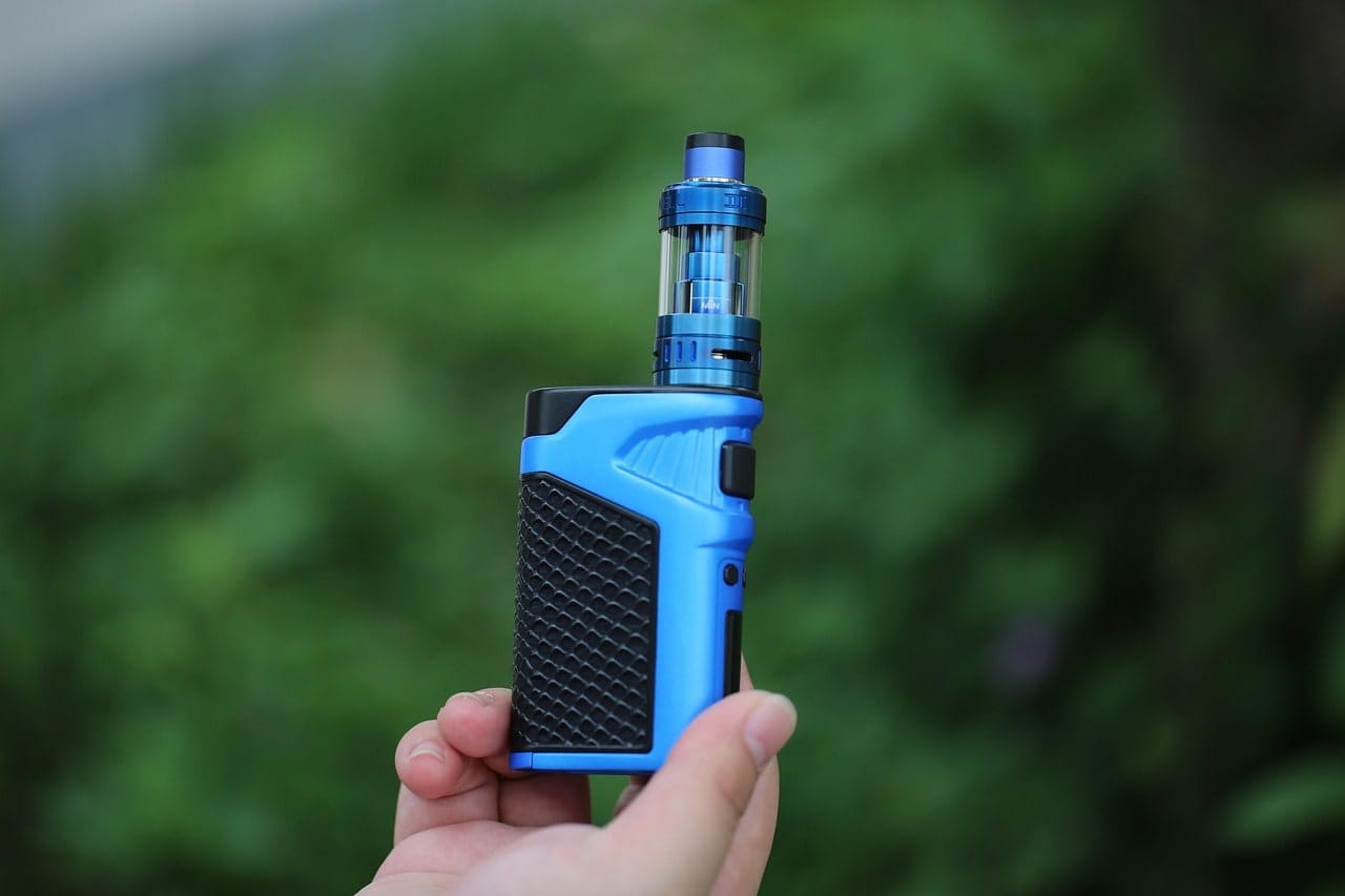 Hand holding a blue vape mod with a clear tank against a blurred green outdoor background – best vape for smokers and vaping enthusiasts.