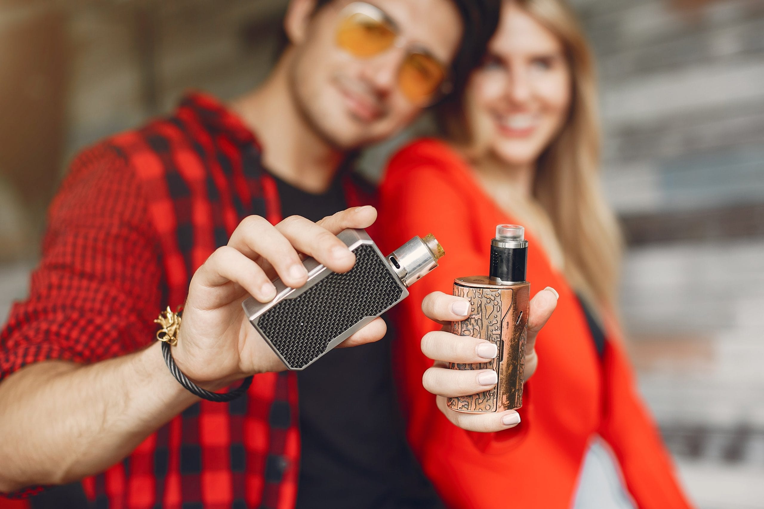Young couple holding vape devices outdoors, showcasing stylish vape mods – ideal for a blog on first-time vaping tips and choosing the right vape.