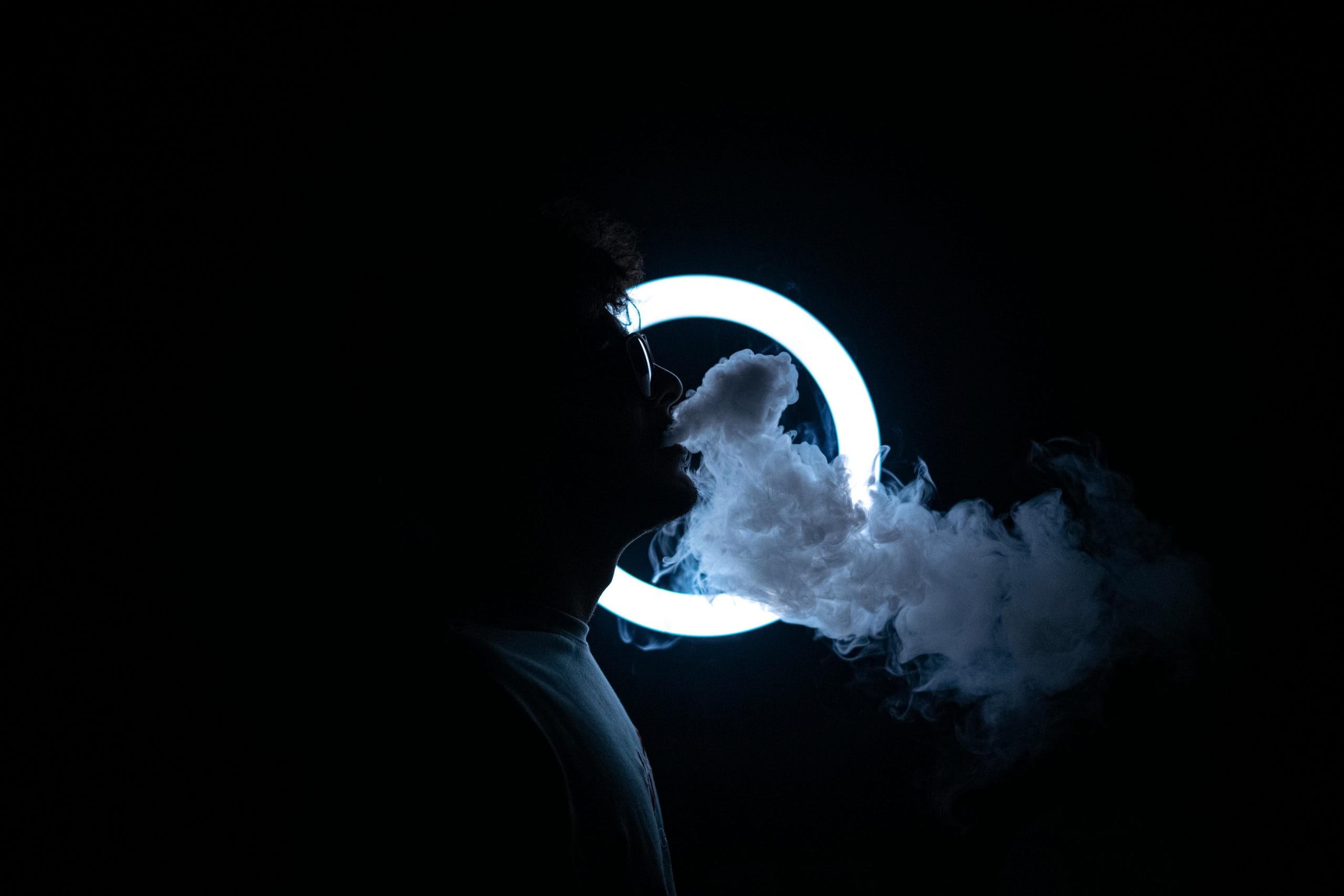 Person exhaling vape smoke with a glowing ring in the background, creating a vape ring effect.