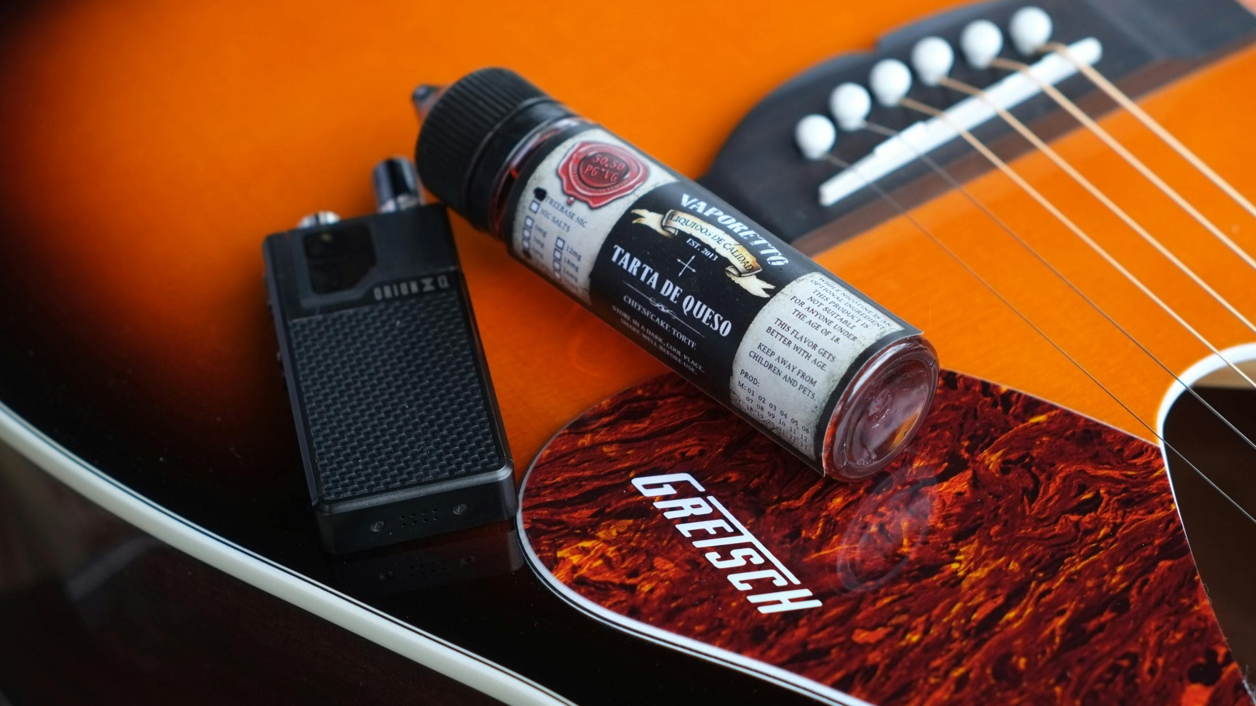 Vape liquid bottle labeled "Vaporetto Tarta de Queso" and a black vape device resting on a Gretsch guitar.